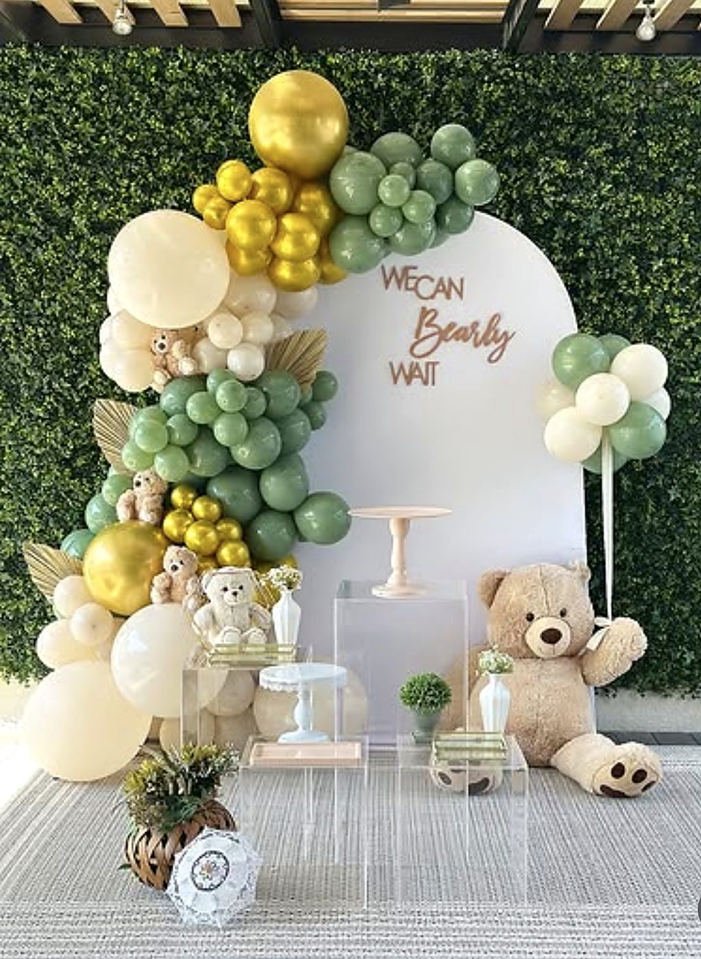 Teddy bear baby shower décor with sage, cream and gold balloons and a white arch backdrop